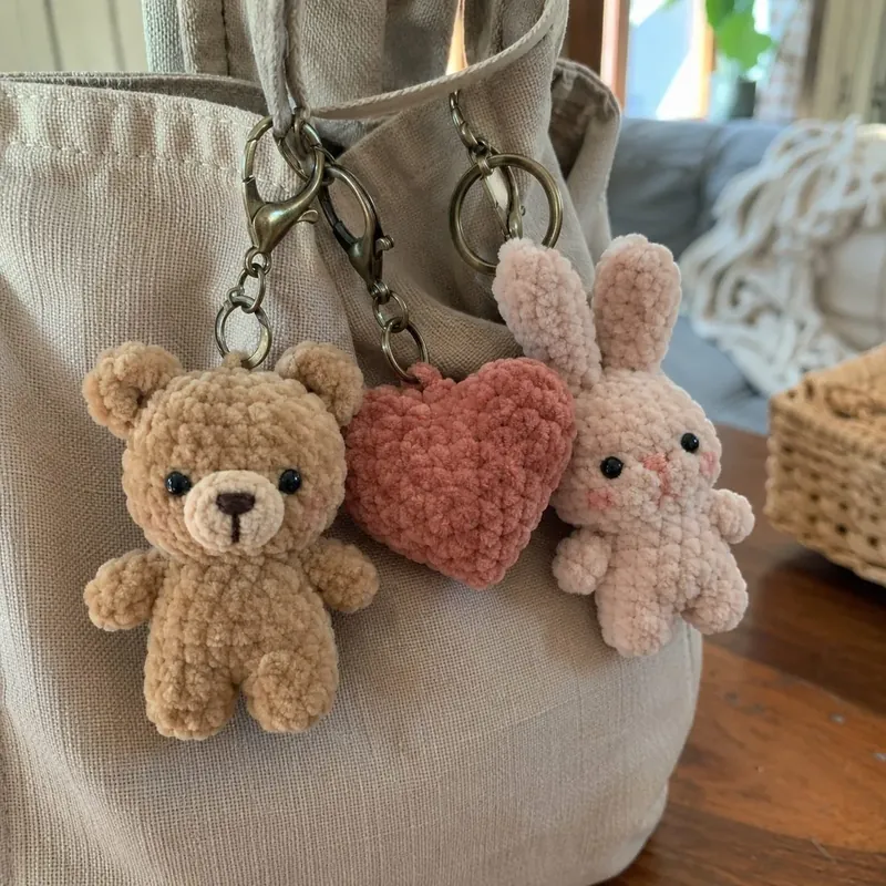 Llaveritos de crochet, un osito, un corazón y un conejito, colgados en un bolso.