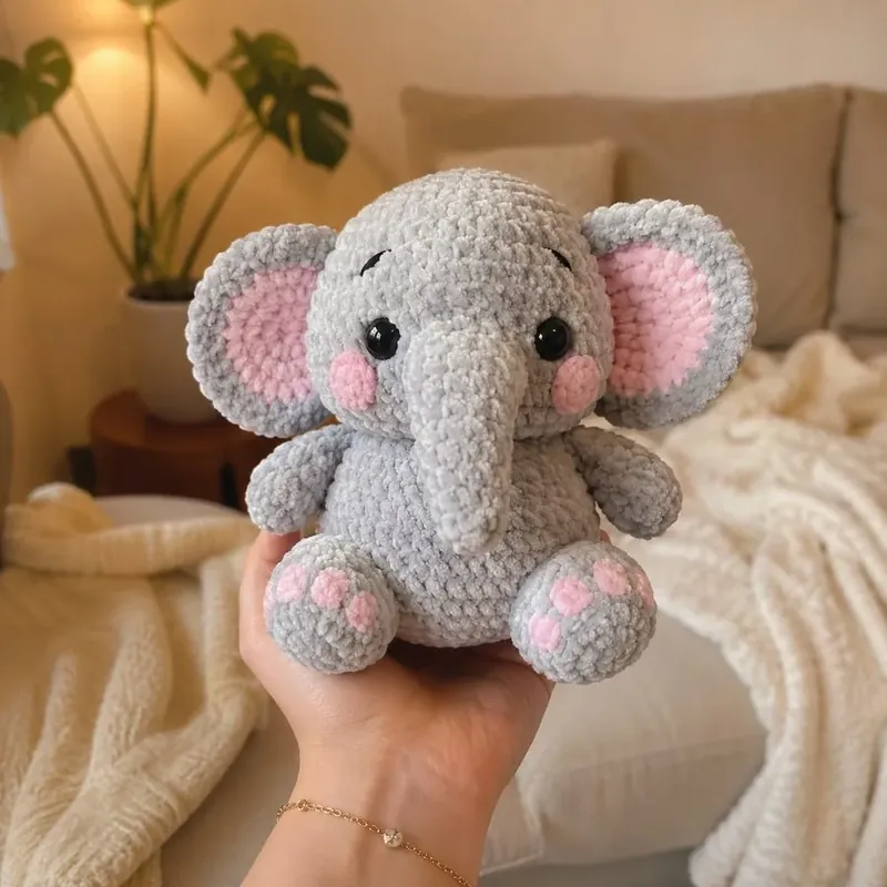 Elefante de crochet en hilo de terciopelo gris con detalles rosa, sostenido en la mano.